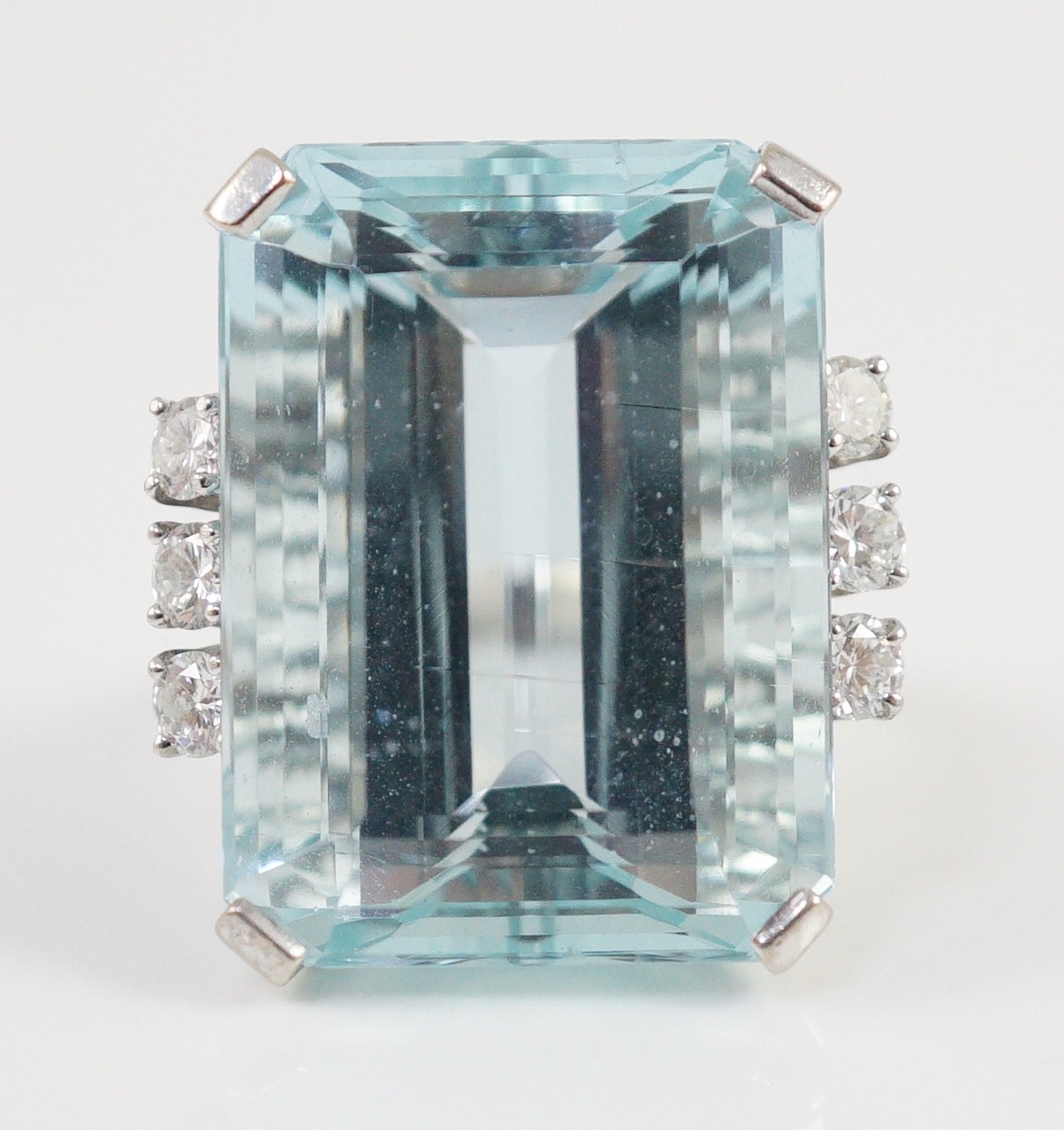A large modern 14k white gold and emerald cut aquamarine set dress ring, flanked by six round cut diamonds